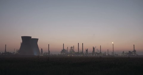 Large oil refinery silhouette against the sunrise. Smoke stacks and steam rising.