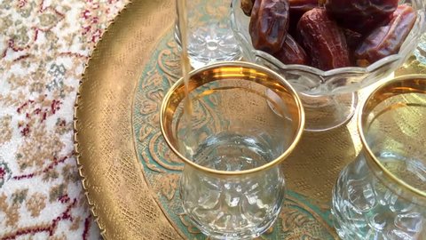 Close up of arabic hot sulemani tea pouring in a traditional golden tea cups, with sweet dates in the background.