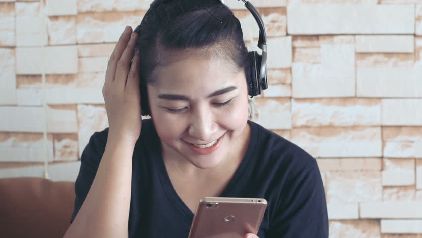 Young asian woman listening music on her smartphone and smiling 