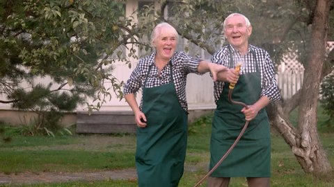 Elderly couple with garden hose. Old people having fun.