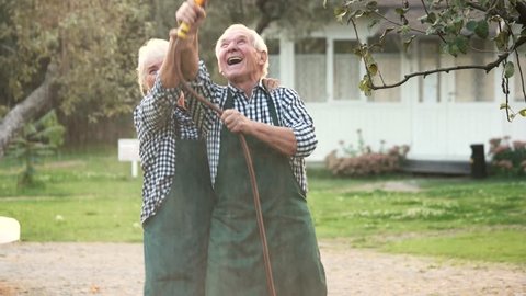 Old couple with garden hose. Cheerful woman and man outdoors.