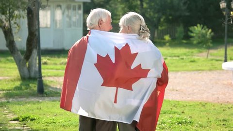 Old couple wrapped in flag. Two people walking, back view. Life in immigration.