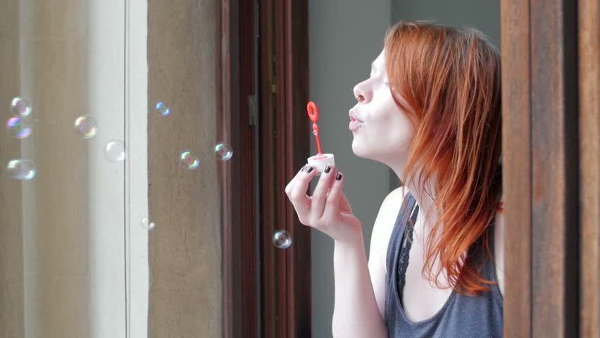 Girl blowing bubbles out the window