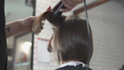 Close-up shot of a woman having her hair straightened in hair salon. Shot in slow motion.