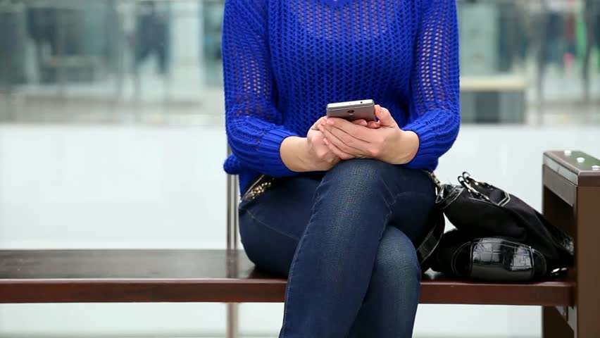 Young sad woman in casual clothes uses modern smartphone while waiting somebody in big modern mall interior. Than puts cell phone into black bag. Real time full hd video footage.