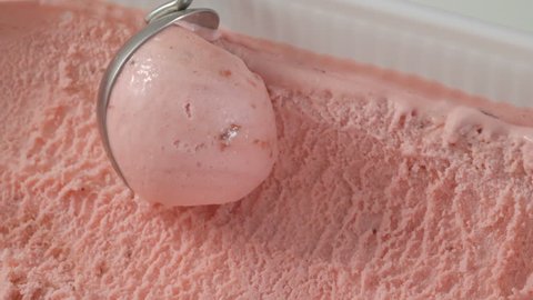 Strawberry ice cream scooped out of container with spoon