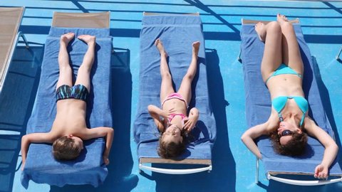 Mother, daughter and son sunbathe in chaise lounges on deck ship