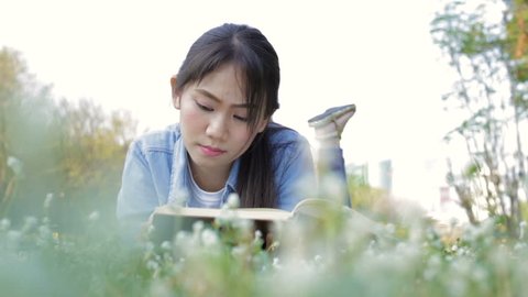 Young teenage girl lying on flower field and reading books on clear sky day