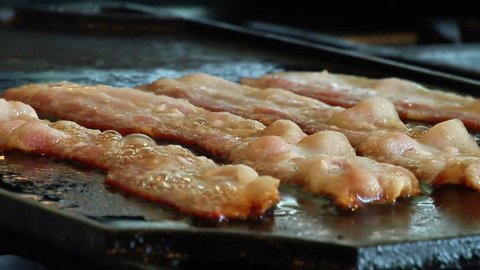 Bacon cooking and sizzling on a cast iron griddle in greasy fat.