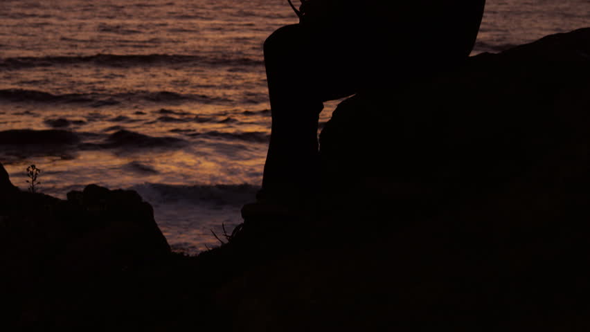 Silhouette of young man putting on sunglasses and staring out at sunset over beach
