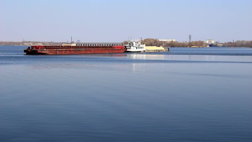 The barge pulls the pontoon and moves along the river towards the dam.