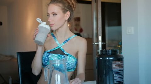 healthy eating woman drinks protein from plastic glass, sport food as part of wellness diet. Beautiful happy blond woman with cup in kitchen. Happy Smiling lady in good mood iwearing blue short top