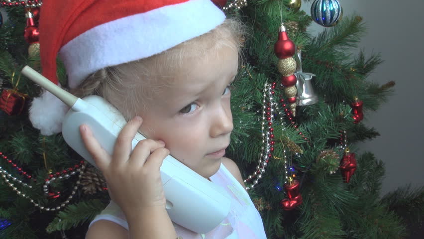 Child Talking on the Phone with Santa Claus by the Christmas Tree, Very Happy Little Girl Speaking on the Phone Near the Christmas Tree