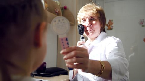 Woman optometrist in clinic checks eyesight at little girl - child's ophthalmology.