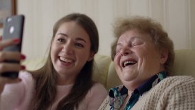 Beautiful granny and her granddaughter are doing selfie, looking at camera and smiling while sitting on couch at home. - Powered by Shutterstock - Get 15% off with code: PIKWIZARD15