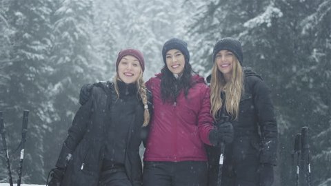 Portrait shot of three young ladies embracing, and smiling at the camera on a snowy day