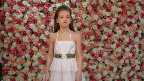 Dancer Girl. Beautiful little girl in white dress is dancing in the studio on a background of a floral wall 