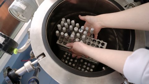 The lab assistant's hand is opening the autoclave lid. Close up contaminated and dirty test tubes with racks in autoclave chamber, microbiology laboratory.