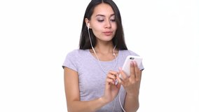 Happy cheerful young asian woman with earphones listening to music from smartphone isolated over white
