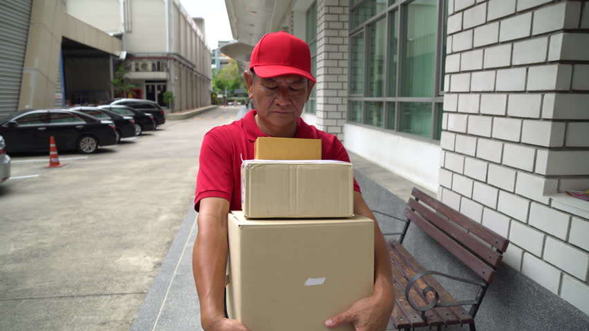 Delivery man holding a cardboard box walking outside building, Gimbal shot.