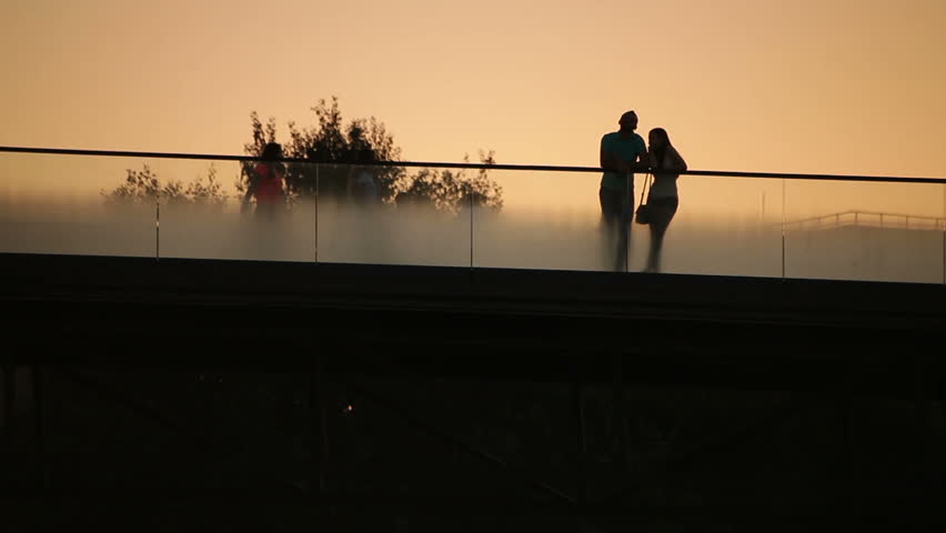Romantic couple at dusk on bridge back lit silhouette.