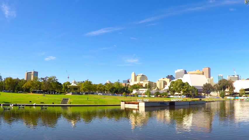 Adelaide Riverbank City skyline from across the Torrens River riverbank with rowers crossing, handheld. 