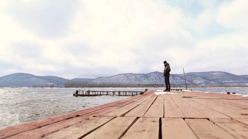 SAMARA, SAMARA REGION/RUSSIA - APRIL 02: Sad pensive man walks on the pier, he sits on the edge of the pier, the mountains on the horizon on April 02, 2017 in Samara