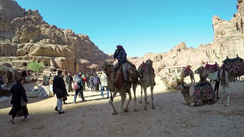 PETRA, JORDAN - circa JAN, 2017: People and camels standing and chewing in front of ruins, ancient city of Petra, Jordan