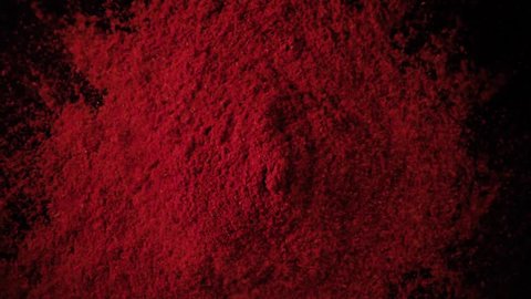 A large amount of paprika red powder drops down on the black table. Slow motion, top view