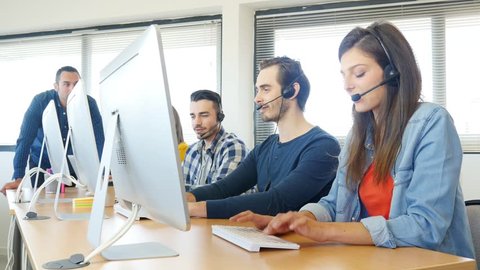 group of four young people with desktop computer in row and headset training with teacher instructor in customer service call support helpline business center