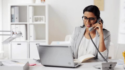 business, technology, communication and people concept - happy businesswoman or secretary with laptop computer and notebook calling on phone and taking notes at office