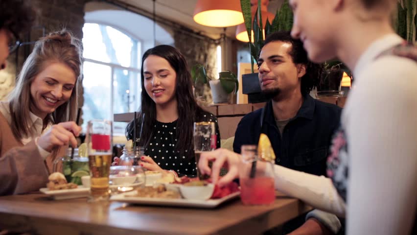 Leisure, food, drinks, people and holidays concept - happy friends eating and drinking at bar or cafe | Shutterstock HD Video #25825391