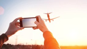 Cinemagraph of woman hands holding smart phone and taking video of big airplane landing in international airport hub at sunset time