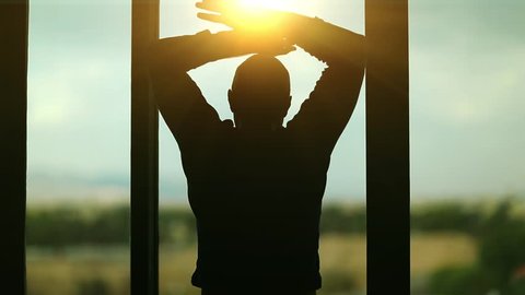 Man opens the curtains in the morning raises his hands and stretch oneself. Young man opens big window curtains and lets the sun light in the room