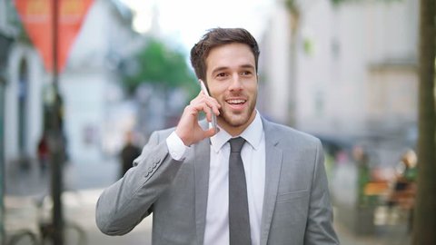 Handsome and young businessman using smartphone in a crowded street. He is talking on the phone and laughing.

