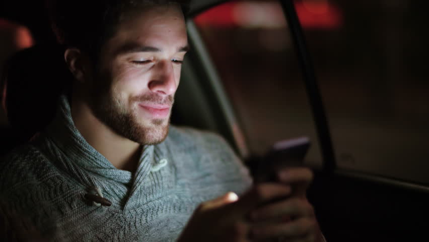 Casual young man using smartphone in a car. He is checking mails, chats or the news online.