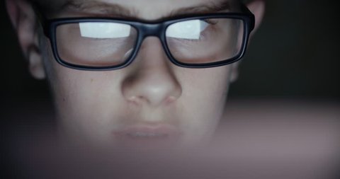 teen boy puberty eye glasses looking at the monitor in a dark room,surfing the Internet, close-up