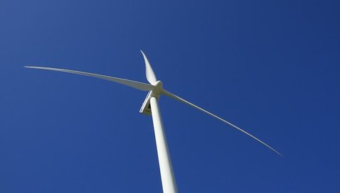 Wind turbine spinning and generating clean and sustainable power in a blue sky.