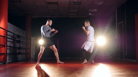 Slow motion. MMA fighters sparring in the ring in darkness.