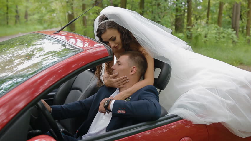 Bride and groom in red cabriolet. Young people kiss each other.