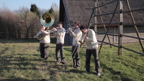 Four musicians make moves to the right and left . Play on wind instruments . Brass Quartet. Synchronous movements of musicians . Wind instrument concert in nature . Concert of musicians in nature .