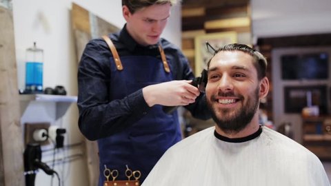 beauty, hairstyle and people concept - happy smiling man and stylist or hairdresser with trimmer doing haircut at hair salon or barber shop