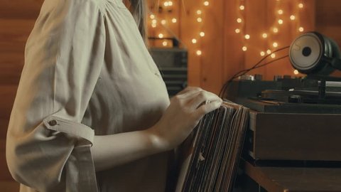 Girl selects Vinyl LP from collection and plays it with turntable. Girl listening to music on headphones Adlı Stok Video