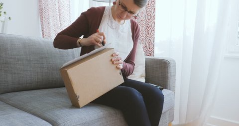 Female blogger vlogger unboxing unpacking cardboard box with from fashion label on home couch