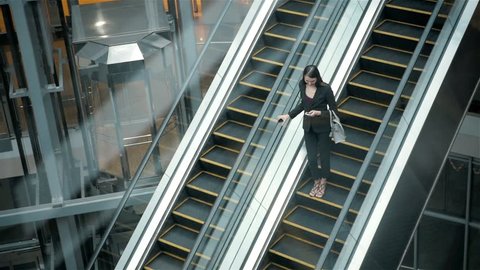Young businesswoman portrait talking at the phone on escalators. Business woman full lenght in shopping mall or office building or airport terminal.