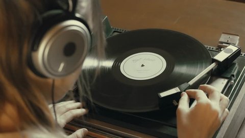 Girl selects Vinyl LP from collection and plays it with turntable. Girl listening to music on headphones
