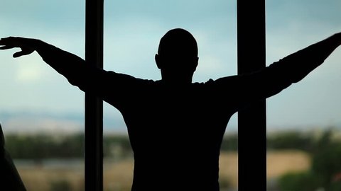 Man opens the curtains in hotel room. Young man opens the curtains in the morning, raises his hands and stretch oneself. Young man opens big window curtains and lets the light in the room