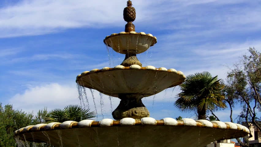 A classic old style tiered fountain with cascading water against a partly cloudy
