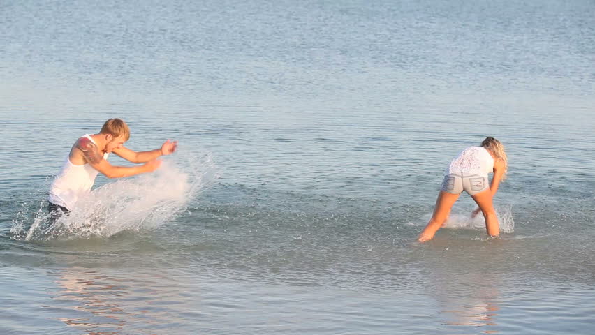 Cheerful couple doing splashes to each other in the summer sea