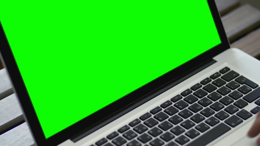 Hand of a man working at laptop computer typing on keyboard on dark desktop. Close up view with green screen. 4k, UHD shot. Laptop on wooden table. Concept of network communications or online shopping